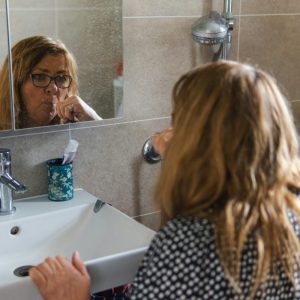 woman brushing her teeth in bathroom mirror