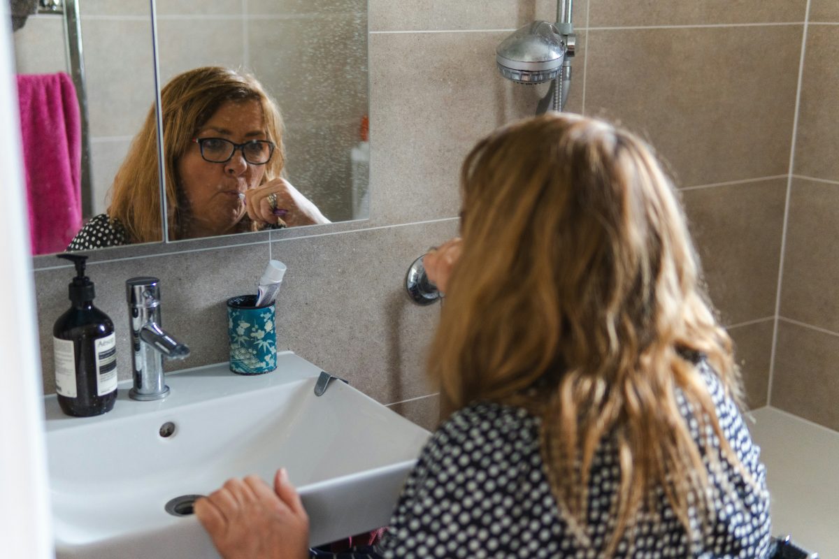 woman brushing her teeth in bathroom mirror