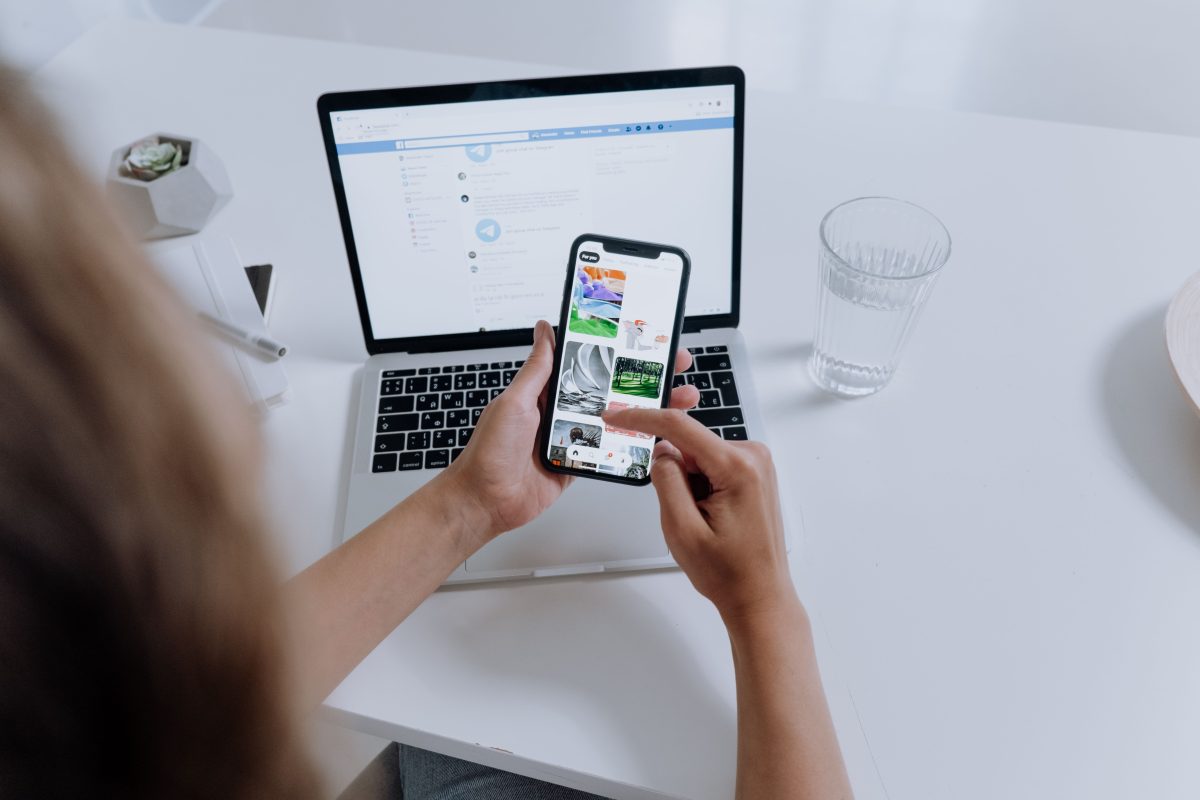 woman scrolling on phone with laptop on table