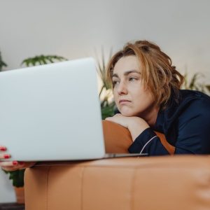 woman in her pajamas looking at a laptop while sitting on the couch