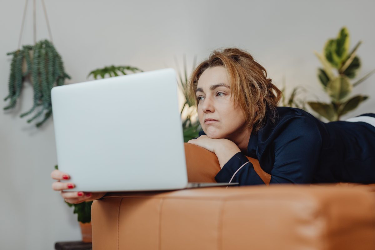 woman in her pajamas looking at a laptop while sitting on the couch