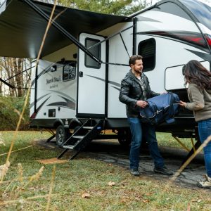 man in black jacket giving box to woman outside of an rv