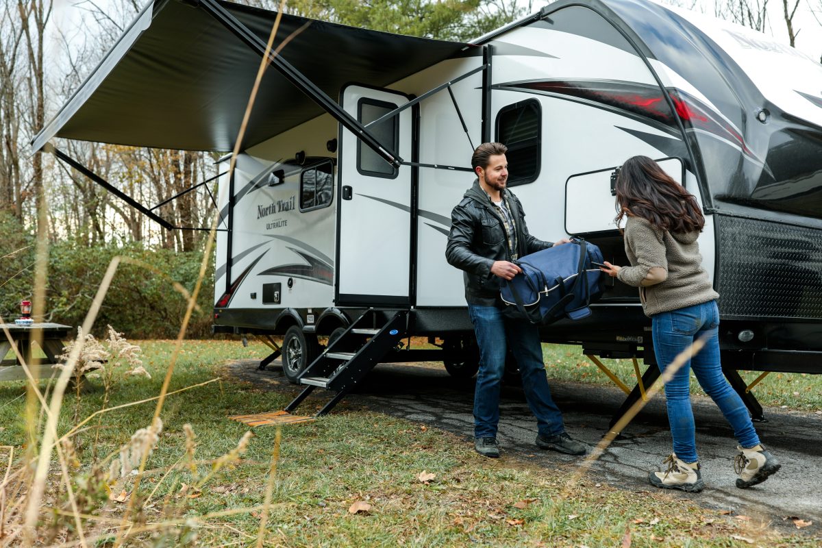 man in black jacket giving box to woman outside of an rv