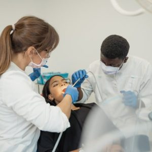 woman sitting in dental chair getting work done with dentist and assistant