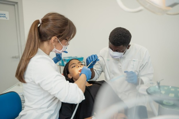 woman sitting in dental chair getting work done with dentist and assistant
