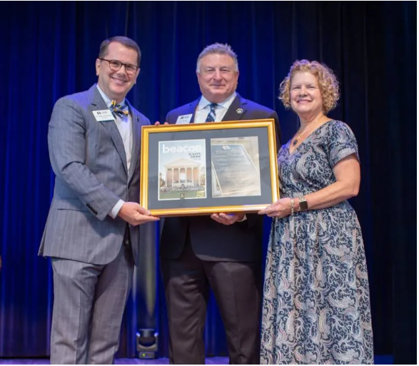 MC President Blake Thompson presents a framed copy of the most recent issue of 'The Beacon,' MC's official alumni and news magazine, to Jim Turcotte, MC vice president and special assistant to the president, in recognition of Turcotte's 32 years of service to the institution. Turcotte's wife, Jenny, is at right.