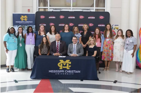 Mississippi Christian University (MC) President Blake Thompson, seated second from right, and Clinton Public School District (CPSD) Superintendent Andy Schoggin, seated second from left, sign the Rising Educator and Arrow Partnership (REAP) agreement on July 30 at Clinton’s Northside Elementary School. Joining them are Mandy Ambrose, seated left, Northside Elementary School principal; Stephanie Busbea, seated right, MC interim provost; and standing directly behind them from left, Jessica Crawley, Northside Elementary School assistant principal, Brittany Ricker, second from left, MC assistant professor of TEL and director of field experience; Rachel Peeples, second from right, chair of MC’s Teacher Education and Leadership program; and Martha D’Amico, right, interim dean of the MC School of Education and Human Science. The group is surrounded by MC students in the first REAP cohort.