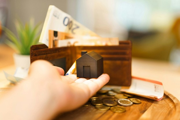 man holding tiny home with wallet in background