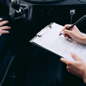 Close-up of a person writing on a clipboard inside a car, showing hands and a gear shift