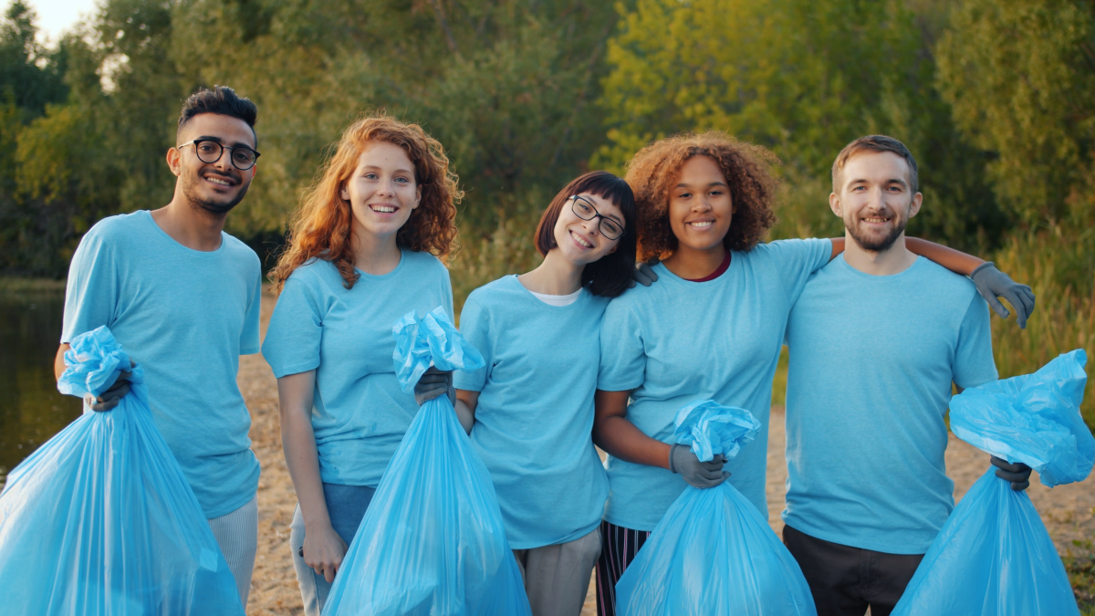 group of people in blue pose for camera while holding blue trash bags