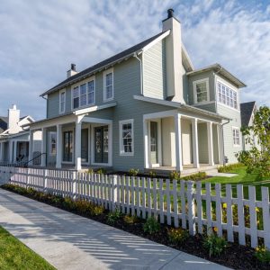 beige green house behind white pickett fence