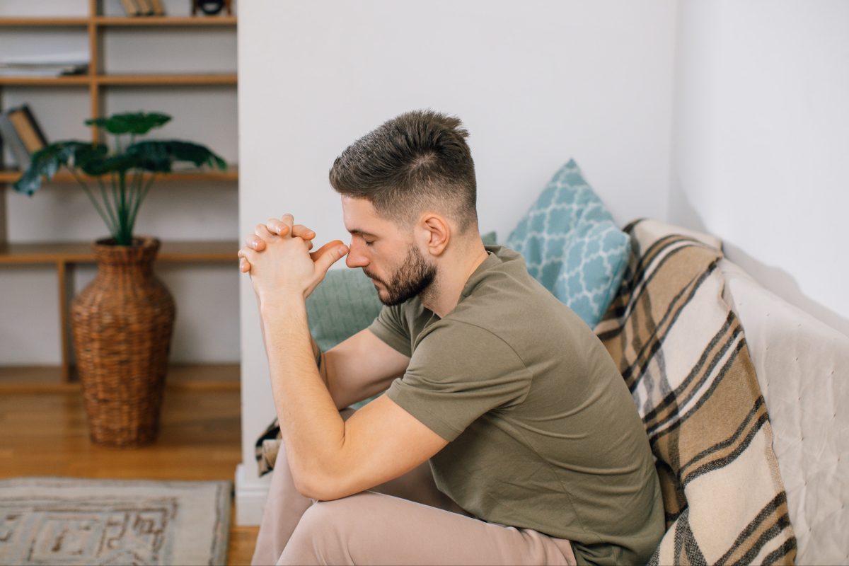 man sitting on couch with hands on head depressed