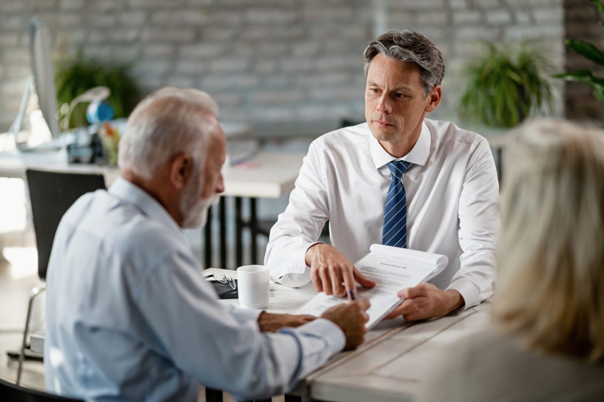 insurance ageny having a meetign with senior clients pointing to signature line on contract
