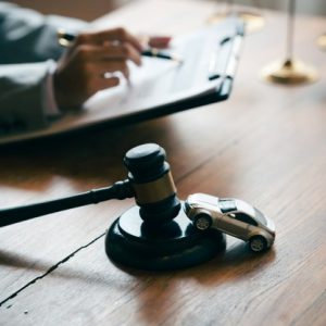 gavel on desk with lawyer in background and tiny car on stand of gavel
