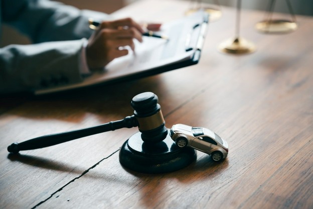 gavel on desk with lawyer in background and tiny car on stand of gavel
