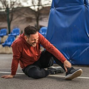 man sitting in road holding an injured ankle