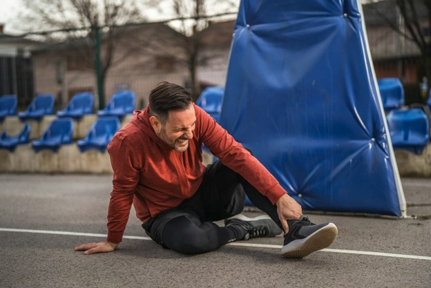 man sitting in road holding an injured ankle