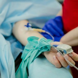 person laying in hospital bed with ivs and someone standing beside them