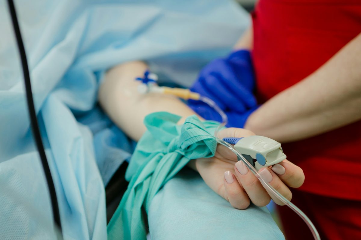 person laying in hospital bed with ivs and someone standing beside them