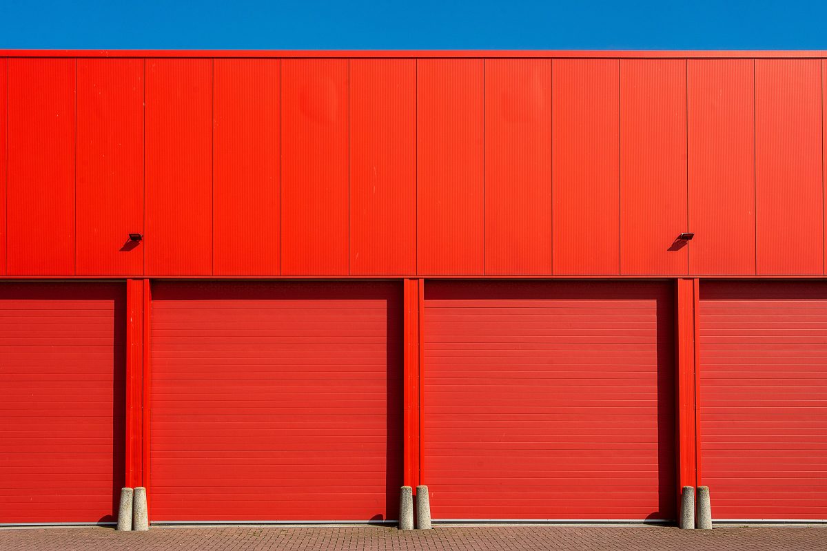 Bright red industrial garage doors in a modern building facade under a clear blue sky.