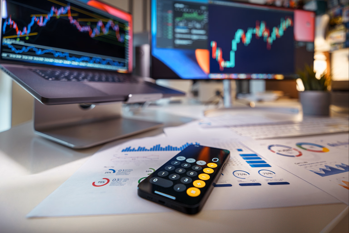 calculator sitting on table with charts and graphs on computer and paper