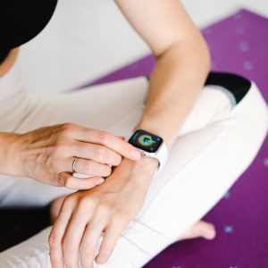Close-up of woman adjusting smartwatch while sitting on a yoga mat, focusing on fitness and technology.
