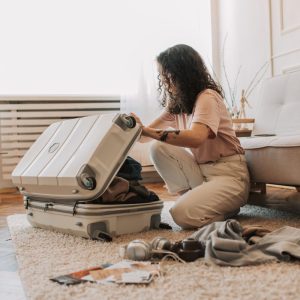 A woman packing her suitcase in a stylish living room, surrounded by clothes and travel accessories