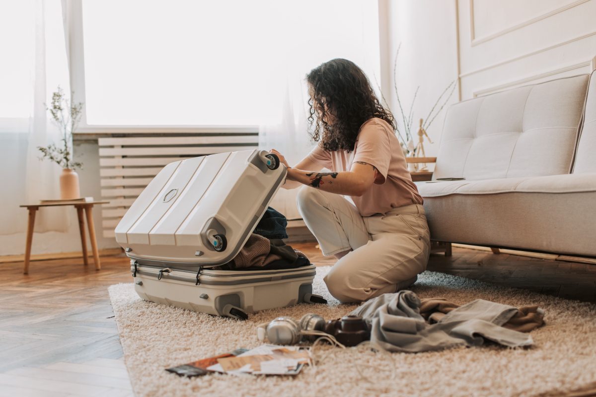 A woman packing her suitcase in a stylish living room, surrounded by clothes and travel accessories