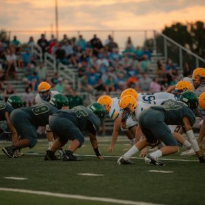 Teams face off in an intense high school football game as the sun sets, adding drama to the scene.