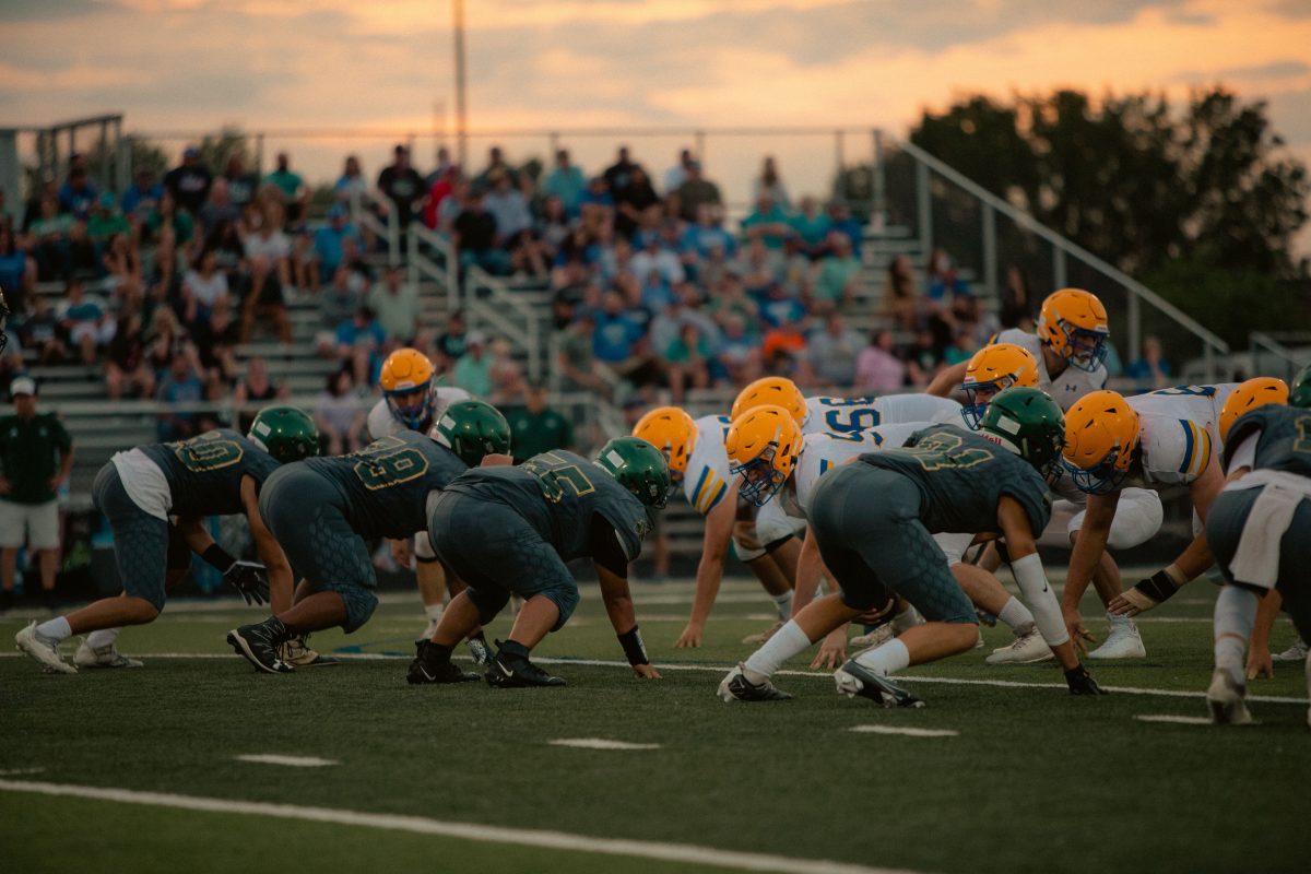 Teams face off in an intense high school football game as the sun sets, adding drama to the scene.