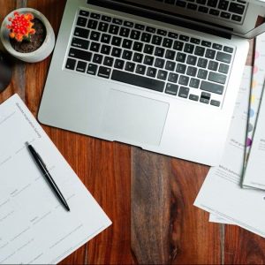 laptop with paperwork sitting on wooden table