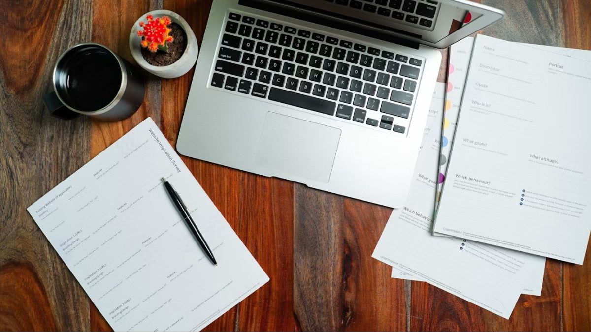 laptop with paperwork sitting on wooden table