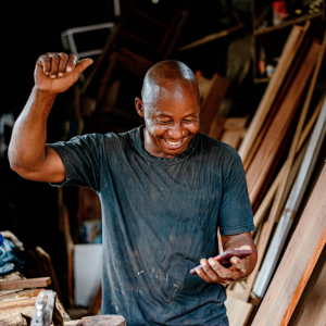 man in blue shirt with boards behind him raising his hand in celebration while looking at phone