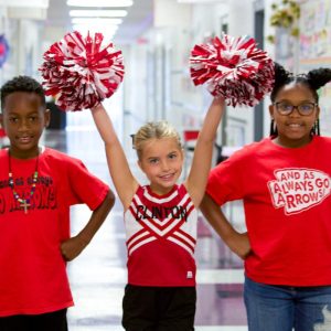 Northside Elementary students in red Arrows shirts cheering with pom-poms in a school hallway