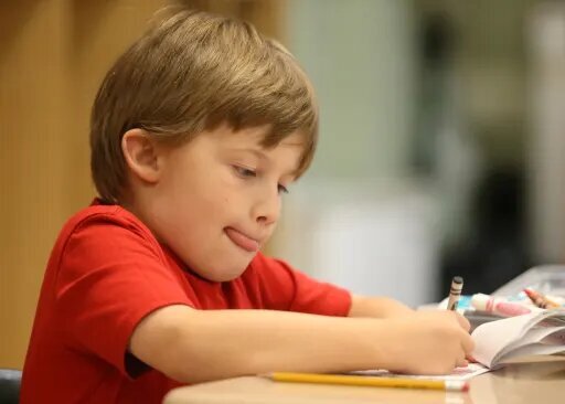 Young student in a red shirt writing at a desk in a classroom