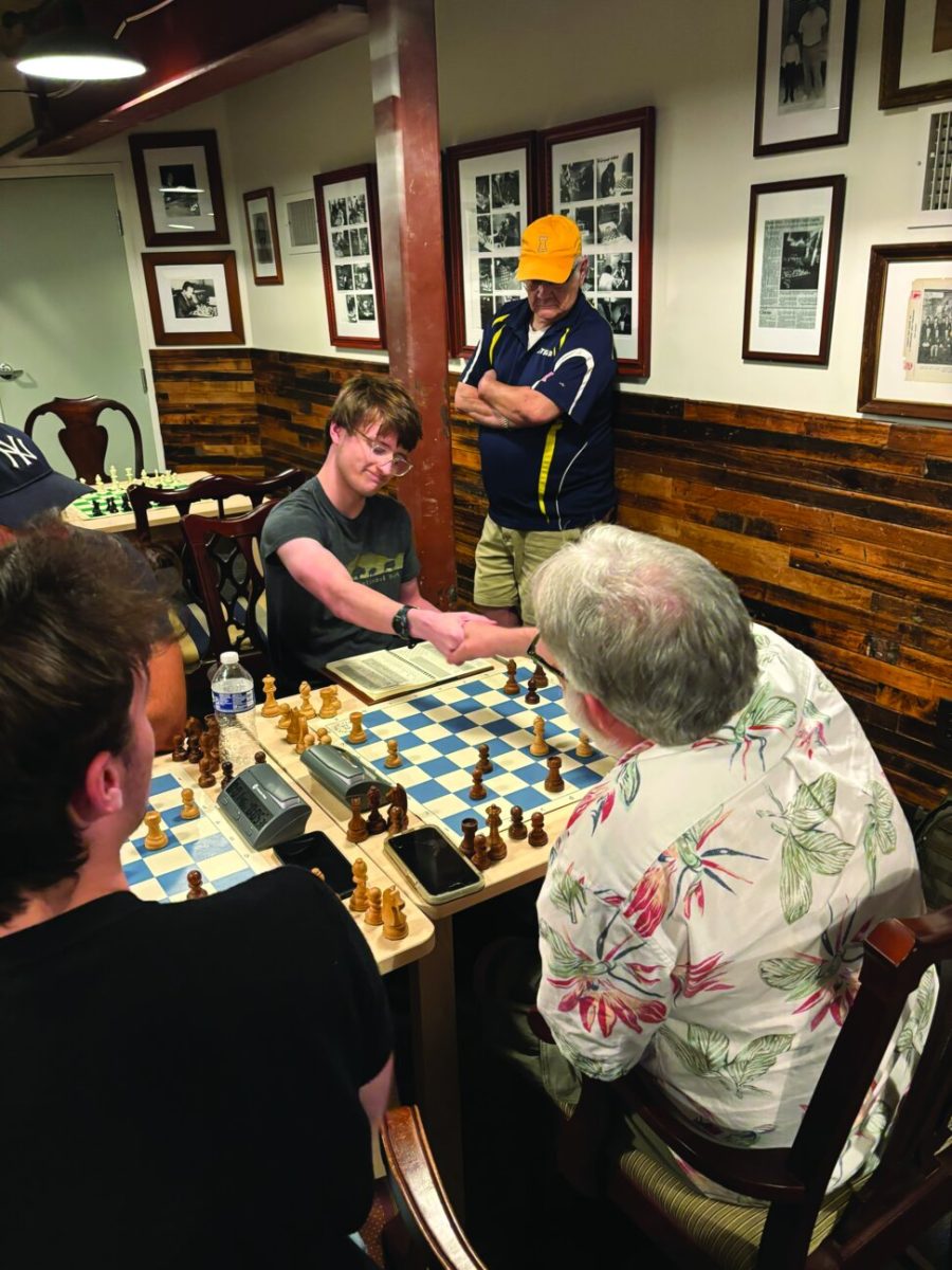 James Dove shaking hands across a chessboard with his opponent at the tournament