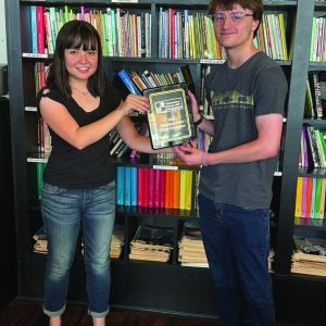 James Dove receiving the first place plaque from the chief tournament director in front of a bookshelf