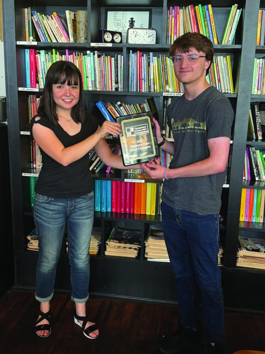 James Dove receiving the first place plaque from the chief tournament director in front of a bookshelf