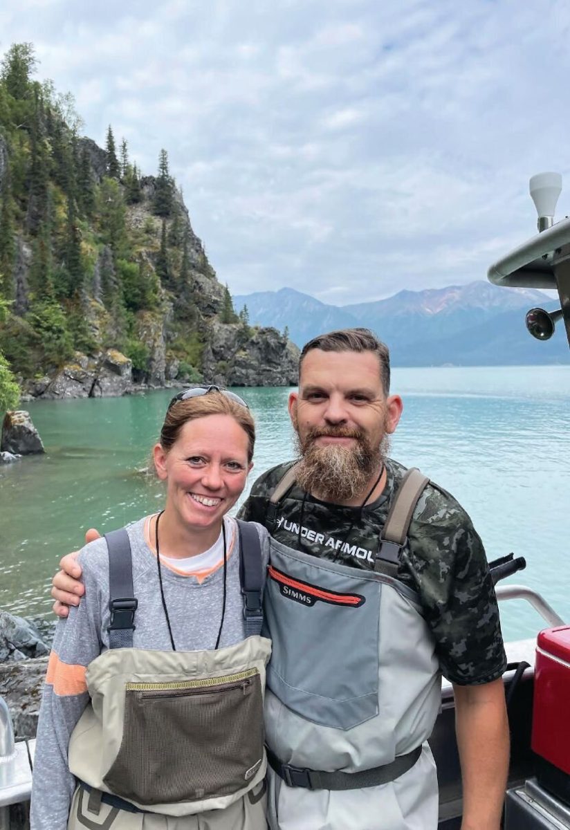 Ryan Groves and his wife in fishing waders beside a lake surrounded by mountains