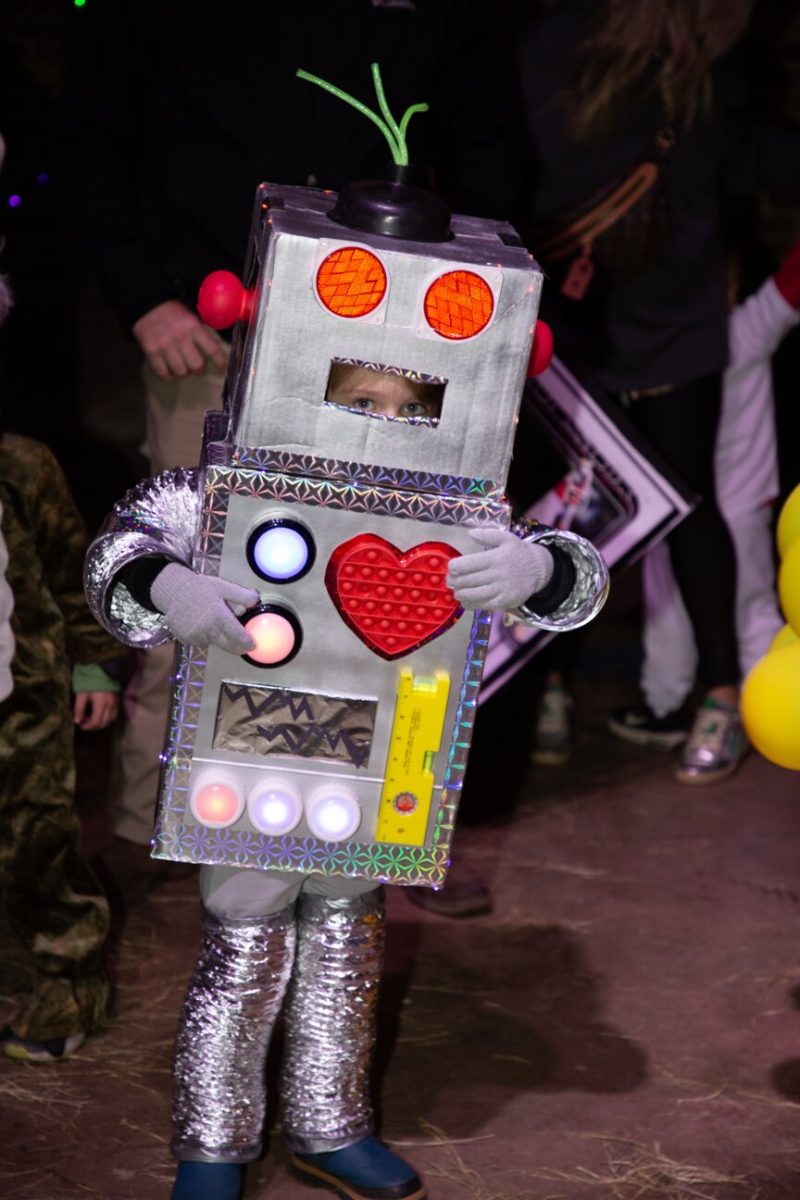 Child in a homemade robot costume with a red heart on the chest at a nighttime Halloween event