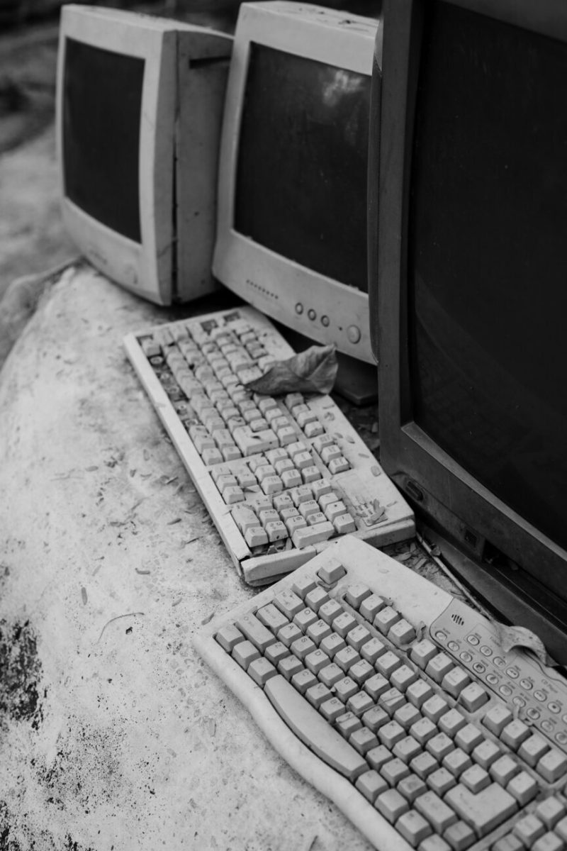 Old computer monitors and keyboards piled together, shown in black and white