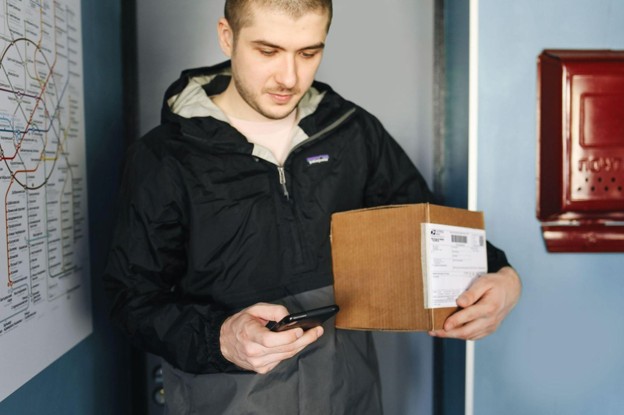 man holding a small delivery box and a phone