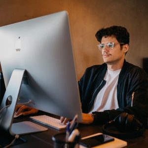 man sitting at computer desk looking at apple computer