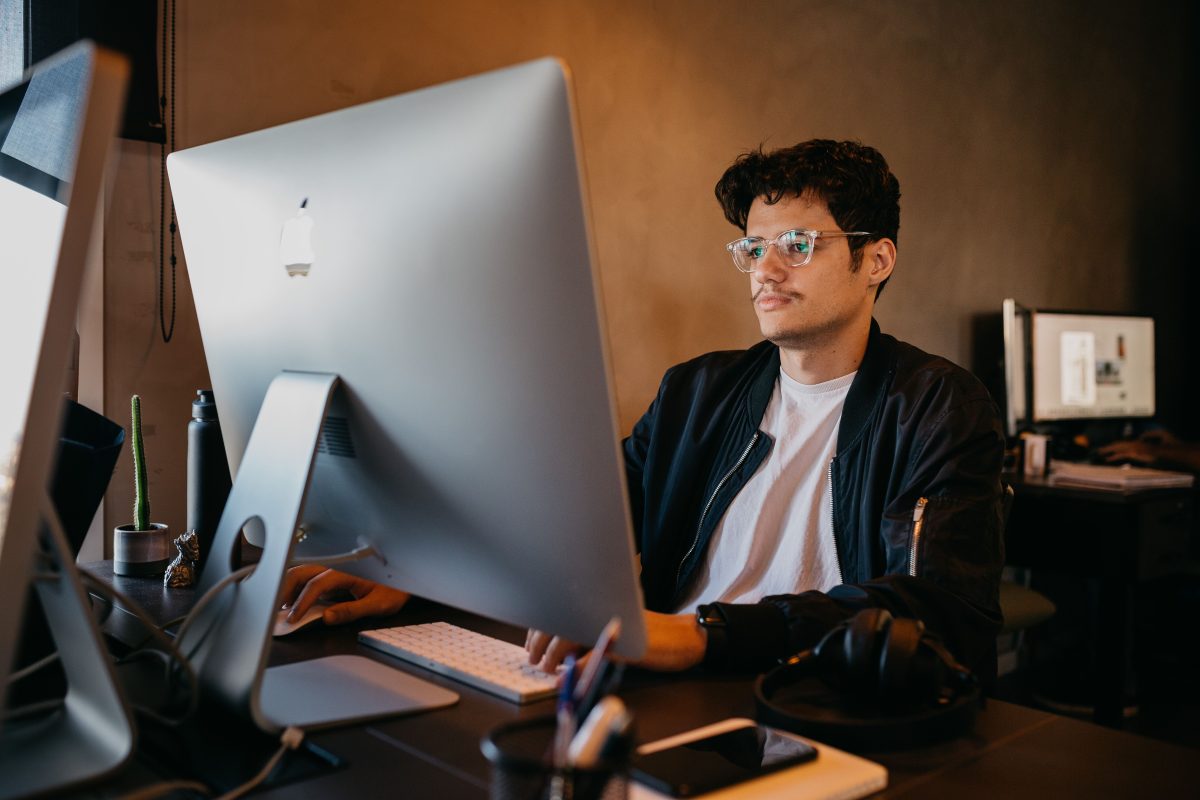 man sitting at computer desk looking at apple computer
