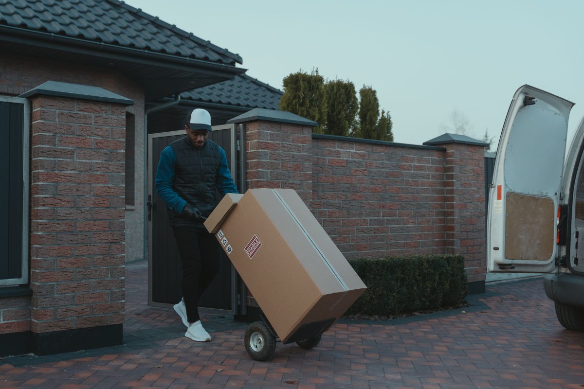 Professional delivery worker transporting package with hand truck in suburban setting.
