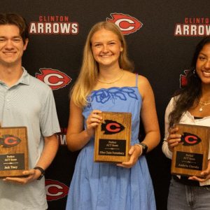 Three Clinton High School seniors holding wooden ACT plaques in front of a Clinton Arrows backdrop