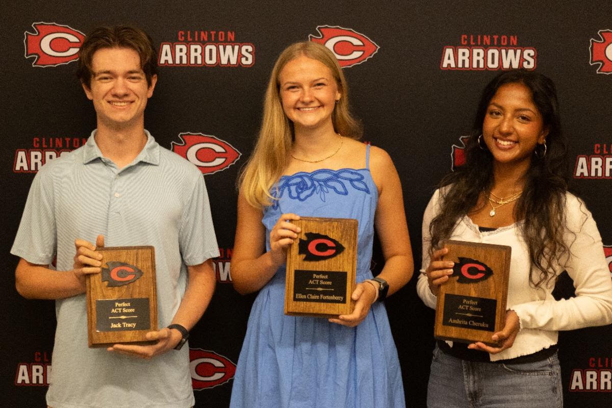 Three Clinton High School seniors holding wooden ACT plaques in front of a Clinton Arrows backdrop