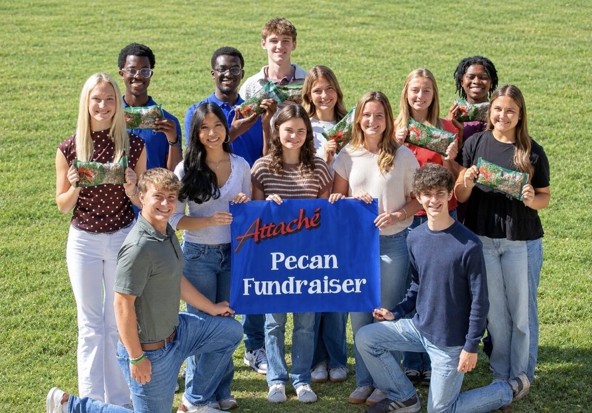Attache’ Show Choir members posing on a lawn with a blue Attache’ Pecan Fundraiser banner