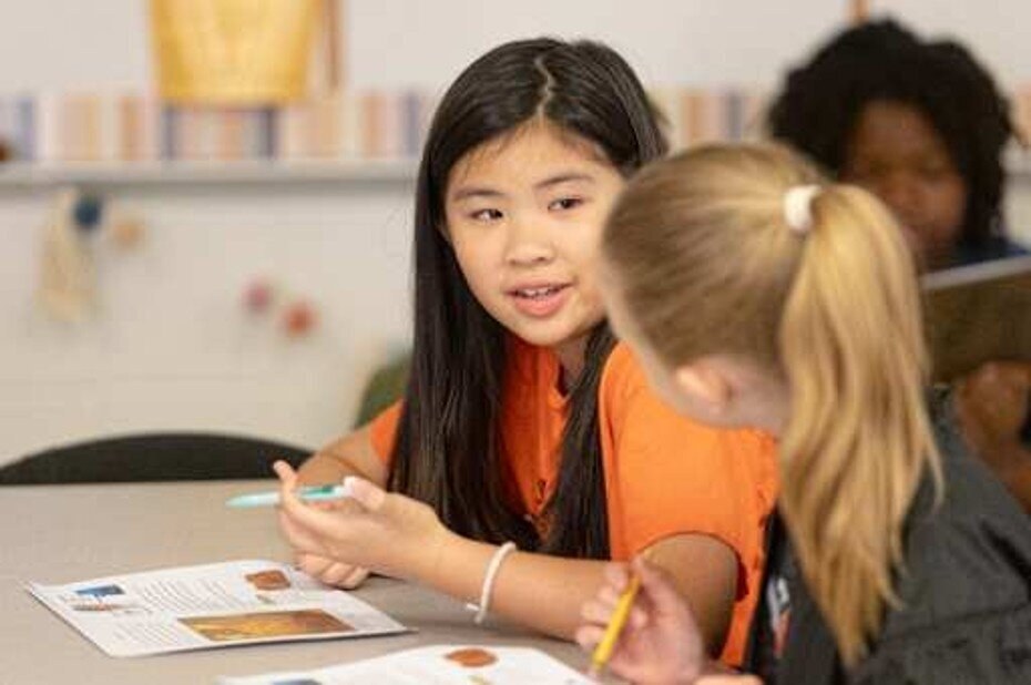 Elementary students at a classroom table working on a project with pencils and papers