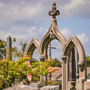 Gothic-style stone monument at Greenwood Cemetery with trees and a partly cloudy sky behind it